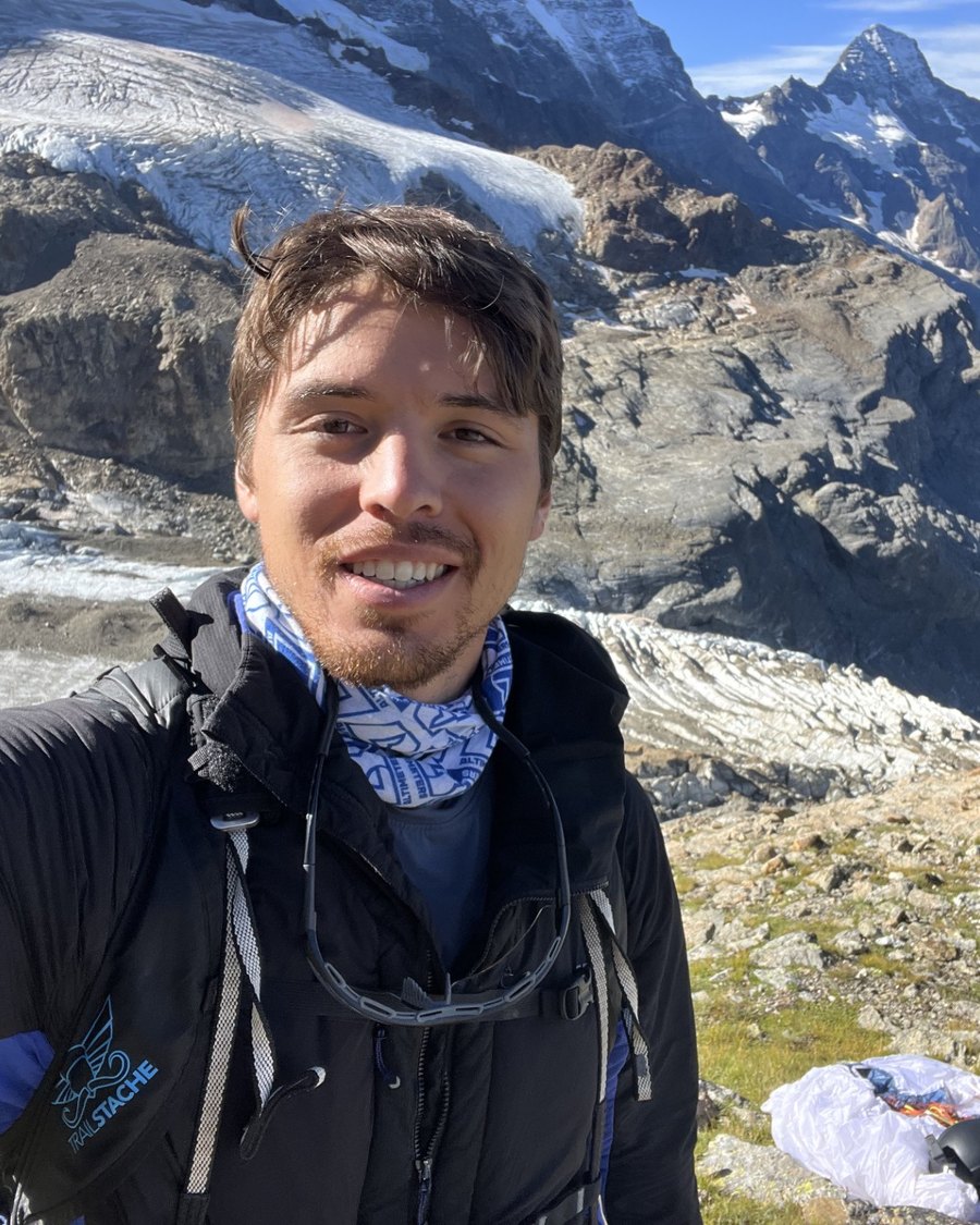 Joseph Ledo-Massey on a ridgeline in the Swiss Alps, glacier and peaks behind him